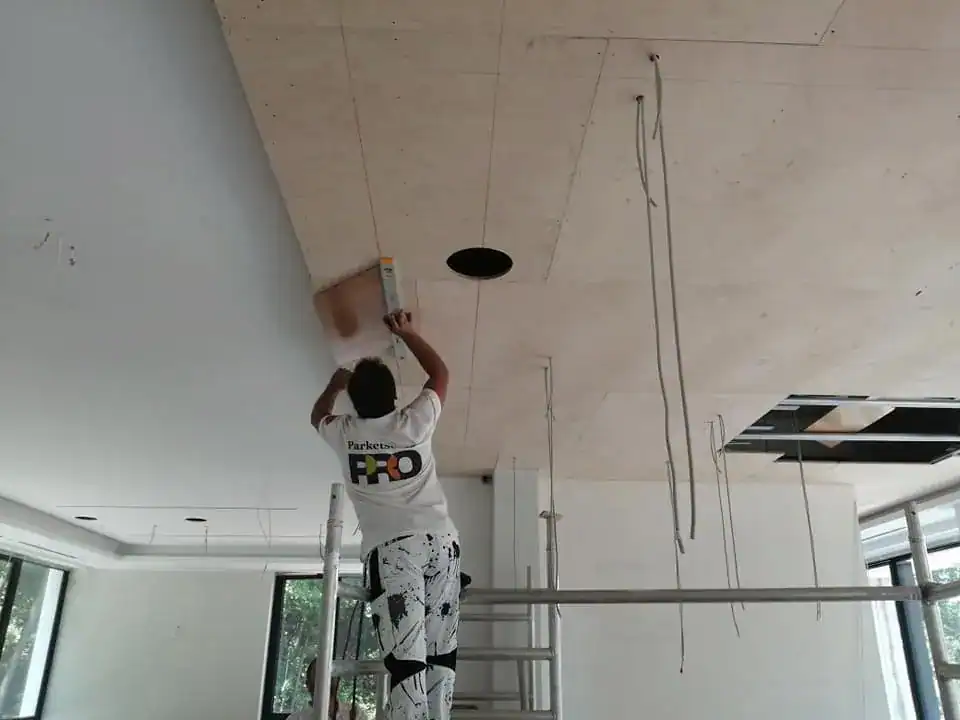 Worker installing suspended ceiling panels during interior finishing project