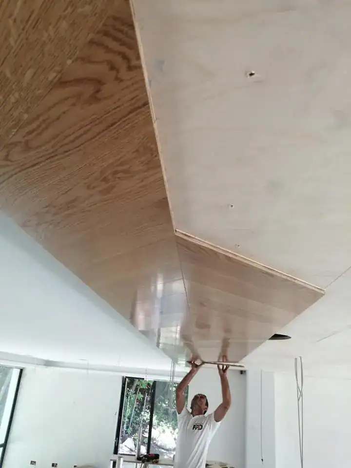 Worker fitting parquet panels onto a ceiling during interior finishing project