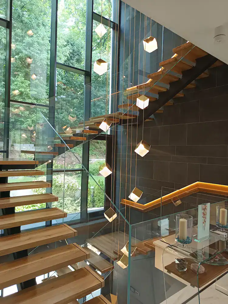 Modern interior staircase with wooden steps, glass railing, and designer lighting – completed construction and finishing project.