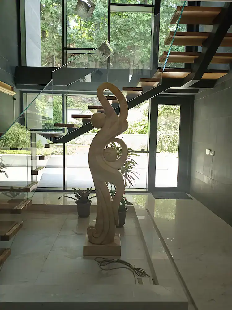 Contemporary interior with wooden staircase, glass railing, marble floor, and artistic sculpture – completed construction and finishing project.